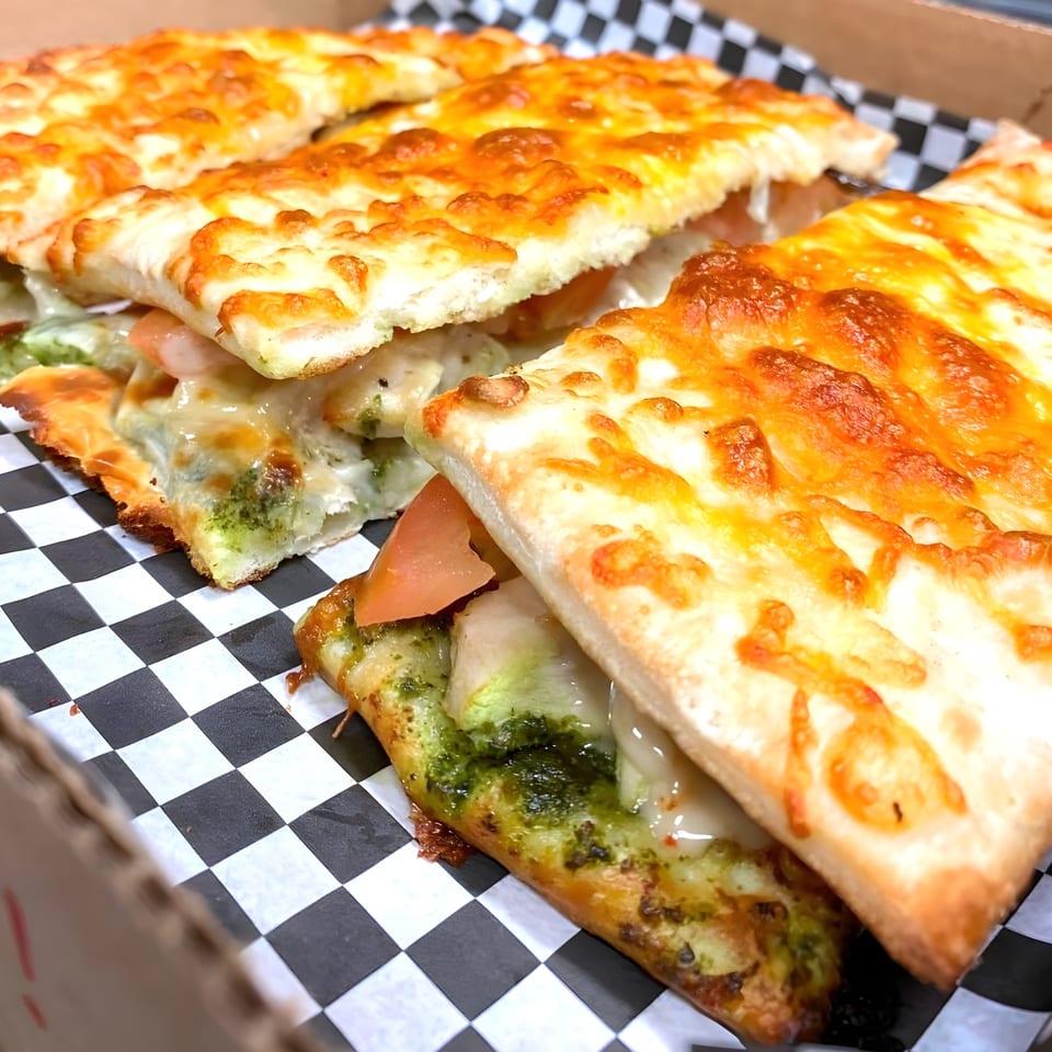 Close-up of Hippo's Chicken, Pizza, Ribs & Fish pesto pizza slices with melted cheese and tomatoes.